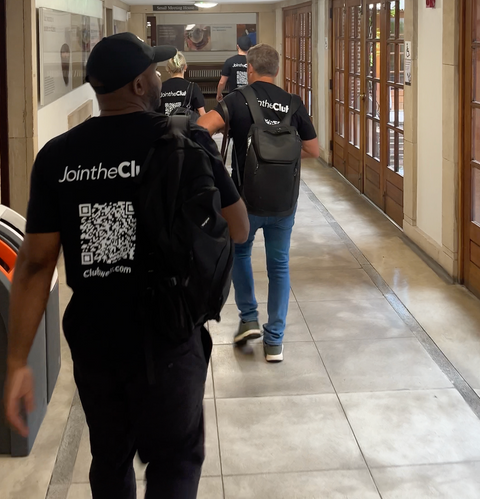 The Clubwell team walking down a hallway wearing black t-shirts with 'JointheClub' branding.