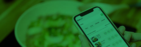 Person holding a smartphone with an app open, blurred plate of food in the background