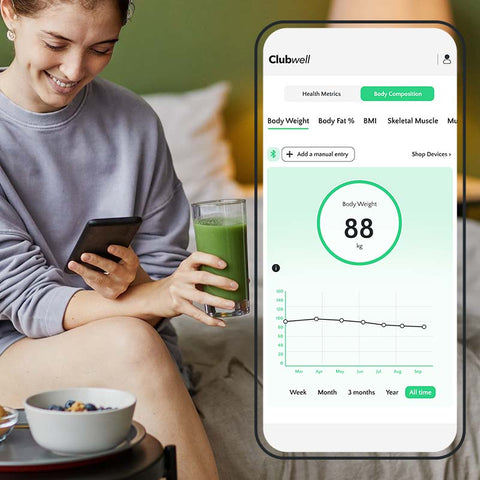 Woman holding a phone with Clubwell app displaying health metrics, holding Green5 drink