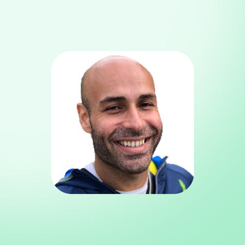 Dr Ali Ibrahim with a beard and smile on a light green background