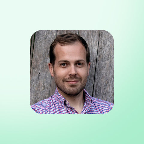 Dr Dan Maggs wearing a checkered shirt against a wooden background