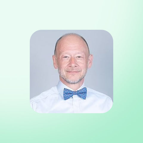 Dr David Unwin wearing a white shirt and blue bow tie against a light green background