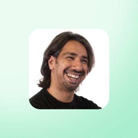 Dr Shan Hussain with long hair smiling against a light green background