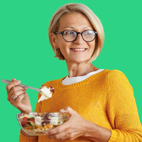 Woman in a yellow sweater eating a salad against a green background