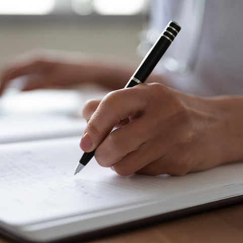 Hand holding a pen over a notebook with a blurred background