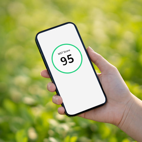 Hand holding a smartphone with MST Score 95 displayed on a blurred green background
