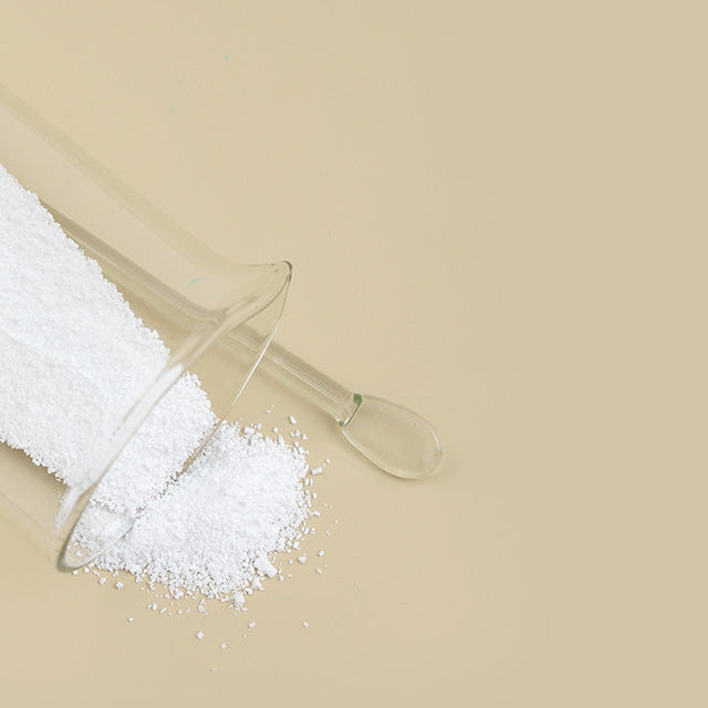 White powder in a clear glass scoop on a beige background