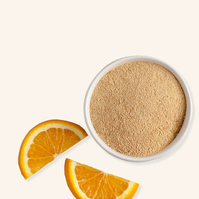 White bowl with brown powder next to orange slices on a white background